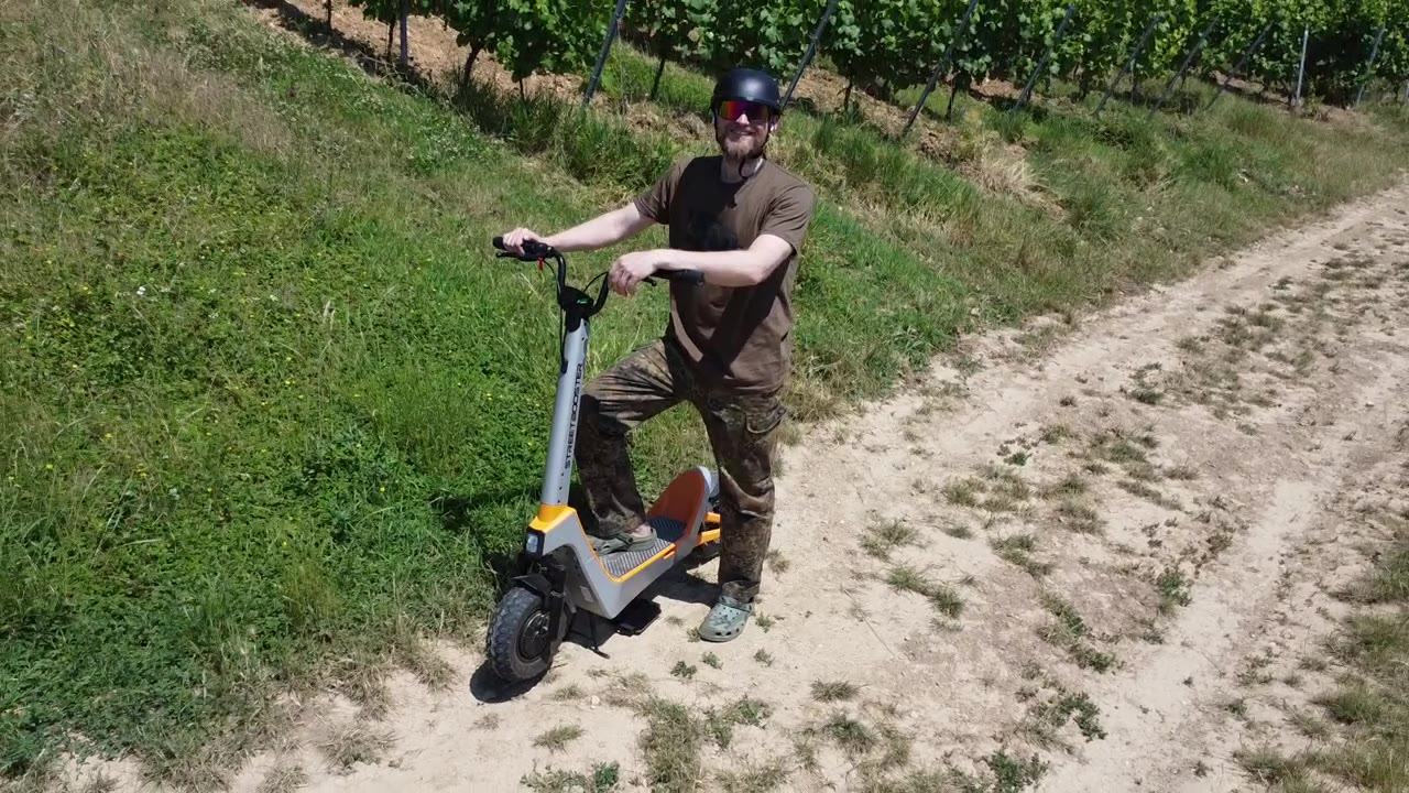 Drohnenaufnahme im Querformat: Fahrer mit E-Scooter auf einem Weg zwischen Weinbergen